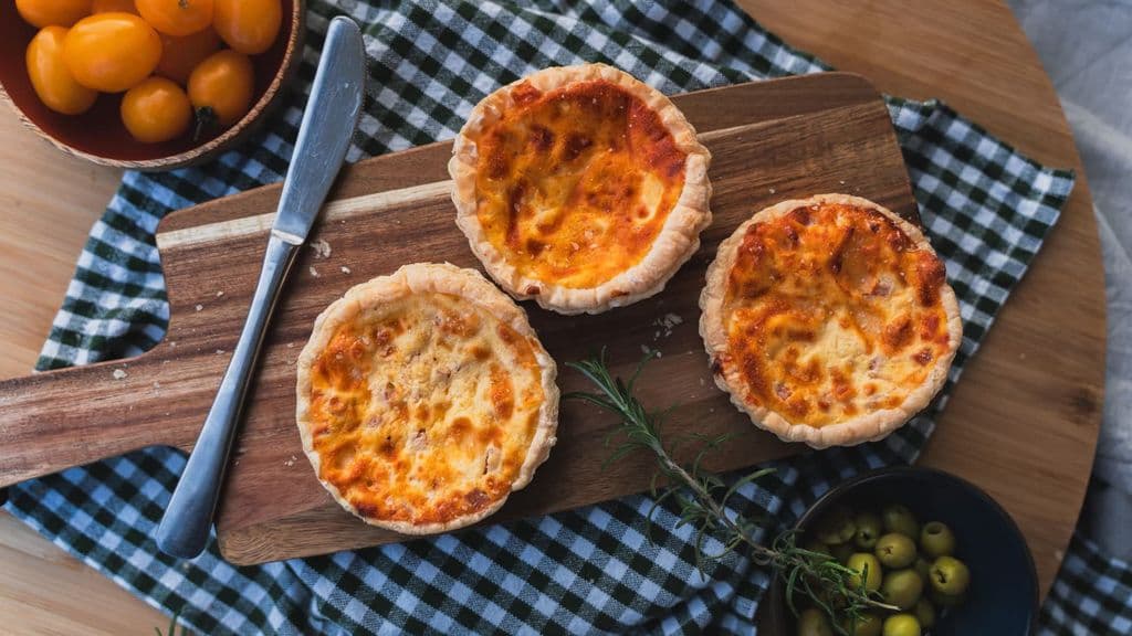Freshly baked mini quiches on a cutting board, by Christian Gazzabini