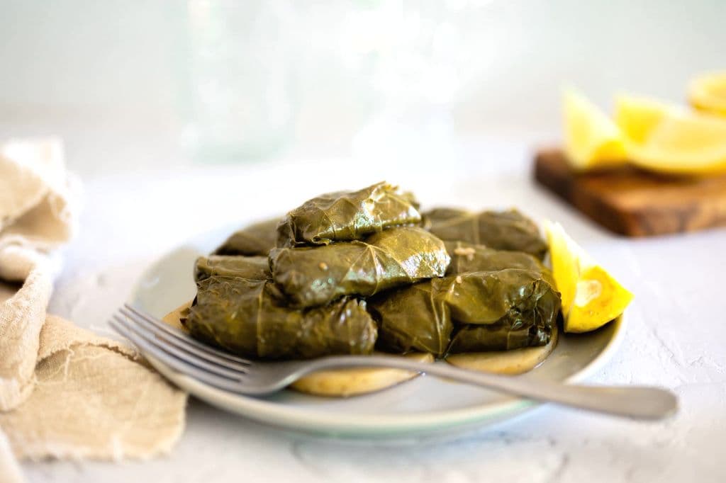 Greek dolmades with lemon wedges on a plate, by eat kubba