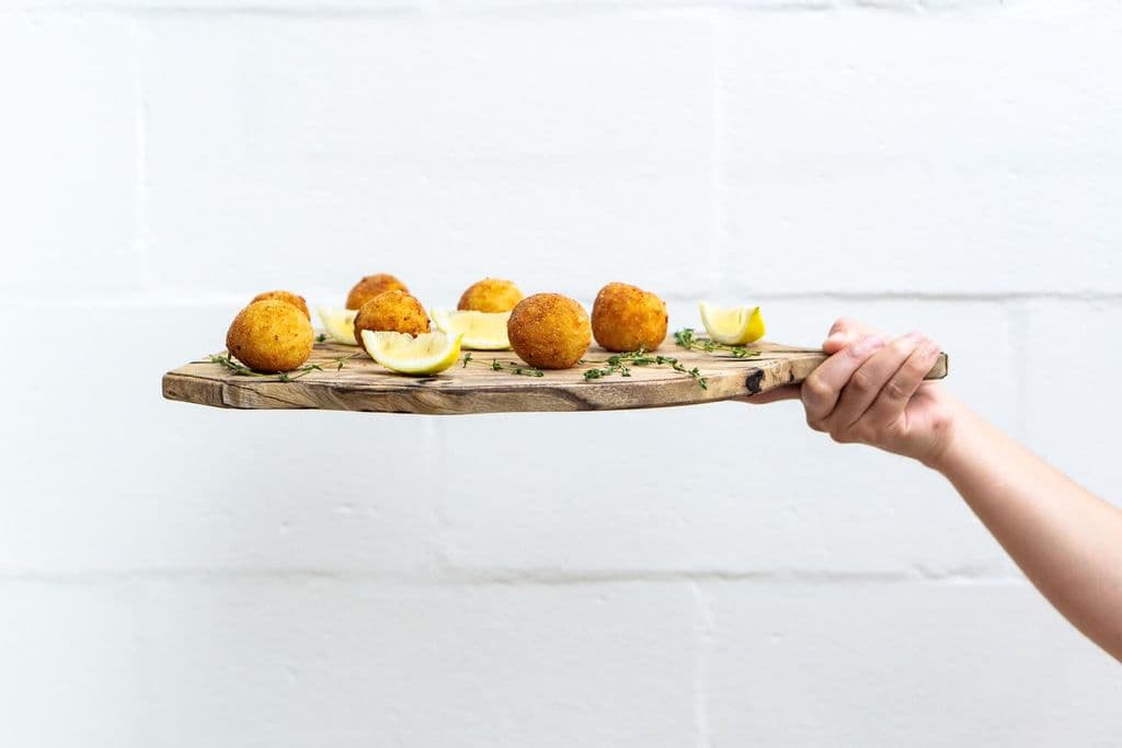 Arancini balls served with lemon slices on a wooden board, by Anna Guerrero