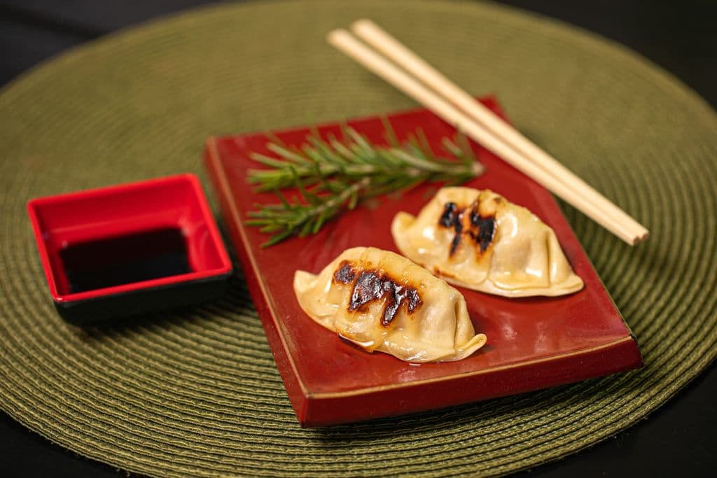 Gyoza dumplings with soy sauce on a red plate, by Lucio Panerai