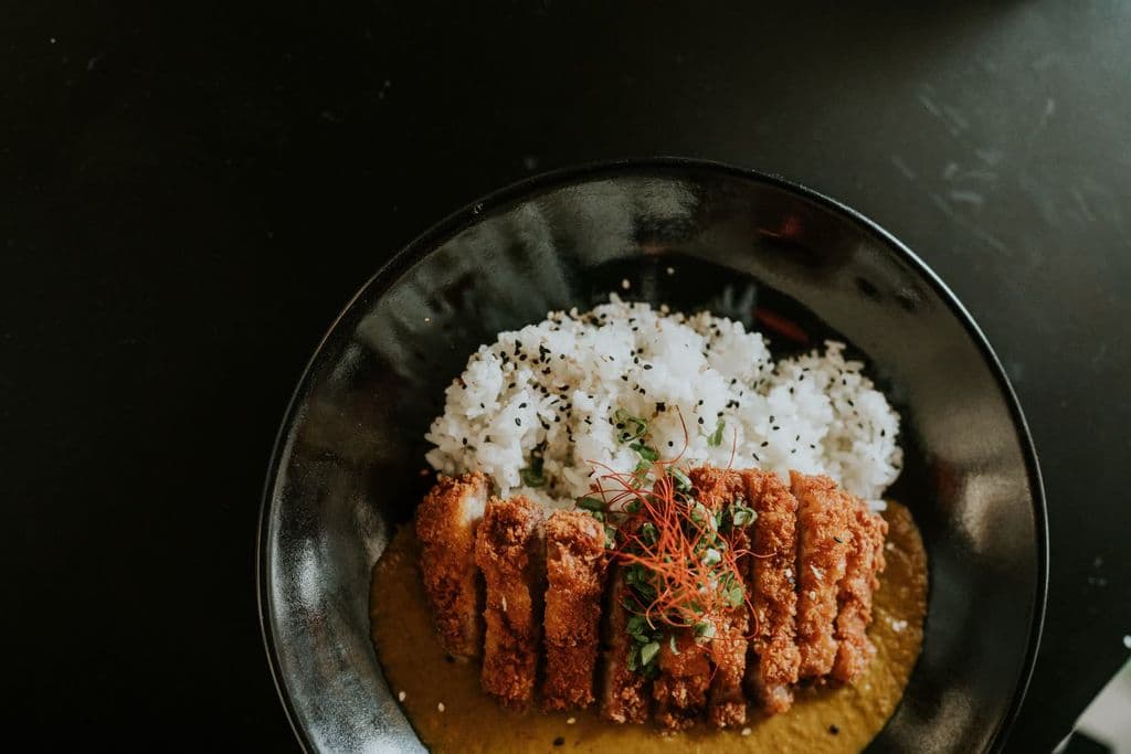 Japanese katsu curry and rice in a black bowl, by Amar Preciado