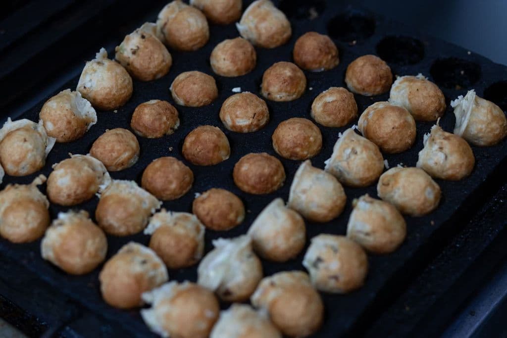 Japanese takoyaki balls cooking on a grill, by Th2city Santana
