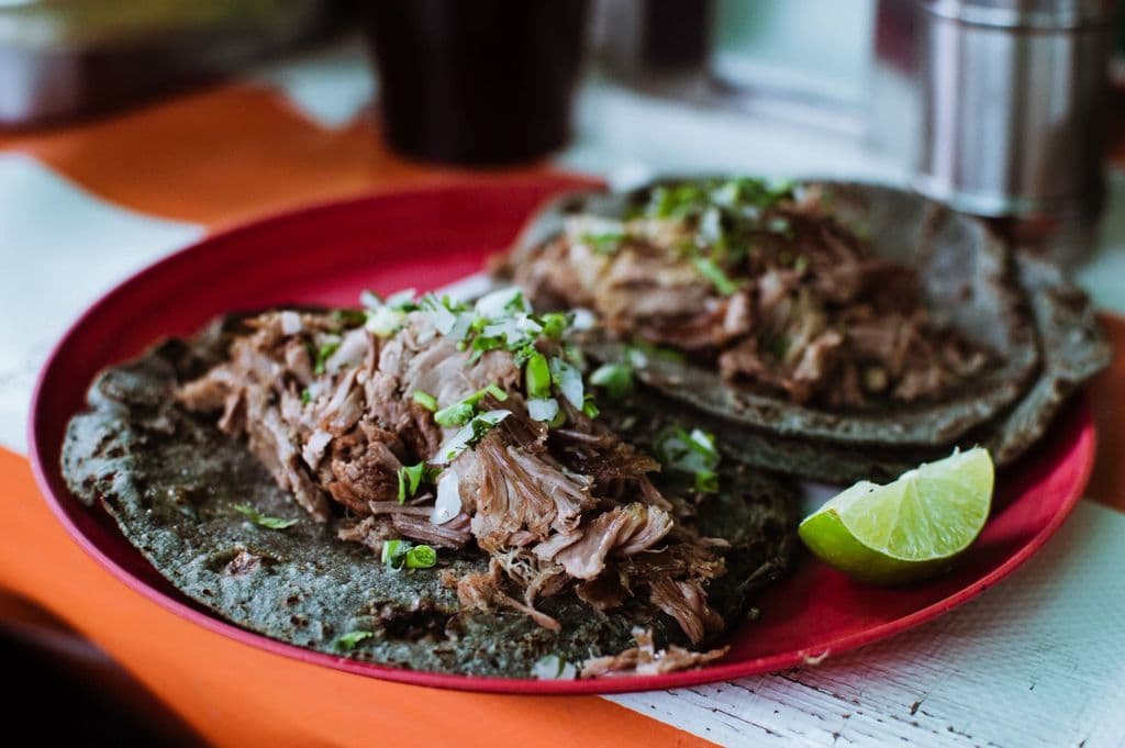 Barbacoa tacos on a red plate with lime, by Susan Flores