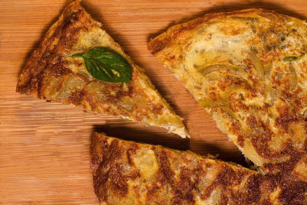 Slices of tortilla española on a wooden board, by Maxi Gagliano