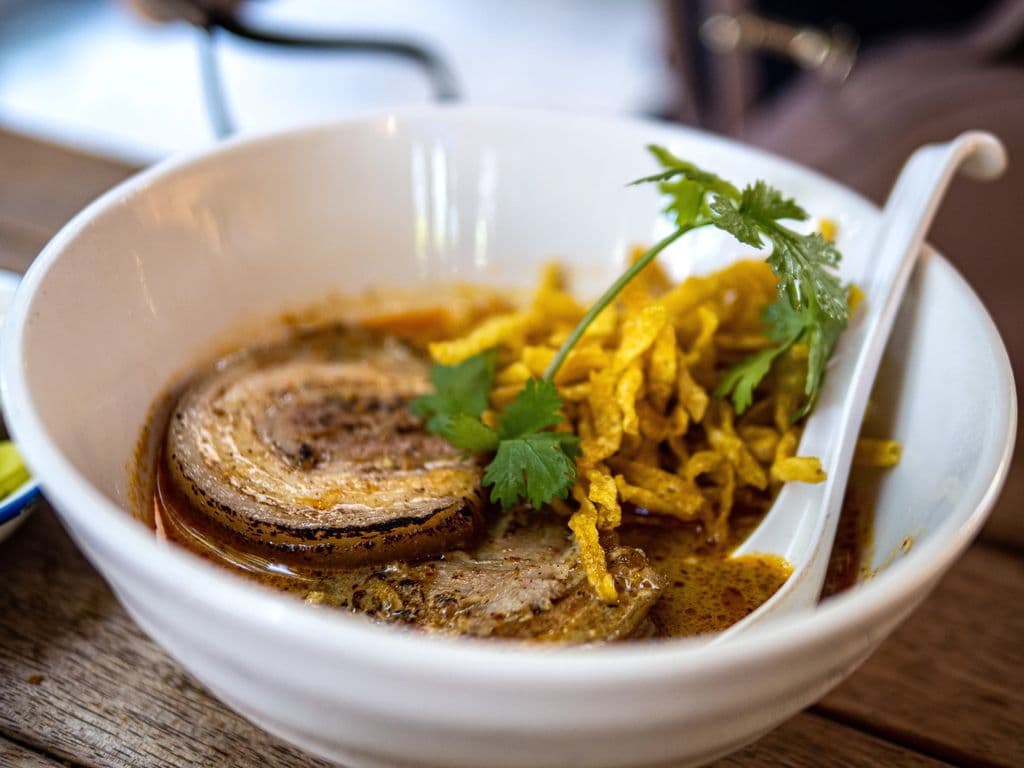 Khao soi curry noodle bowl with herbs, by Likeboss lertpongsaporn