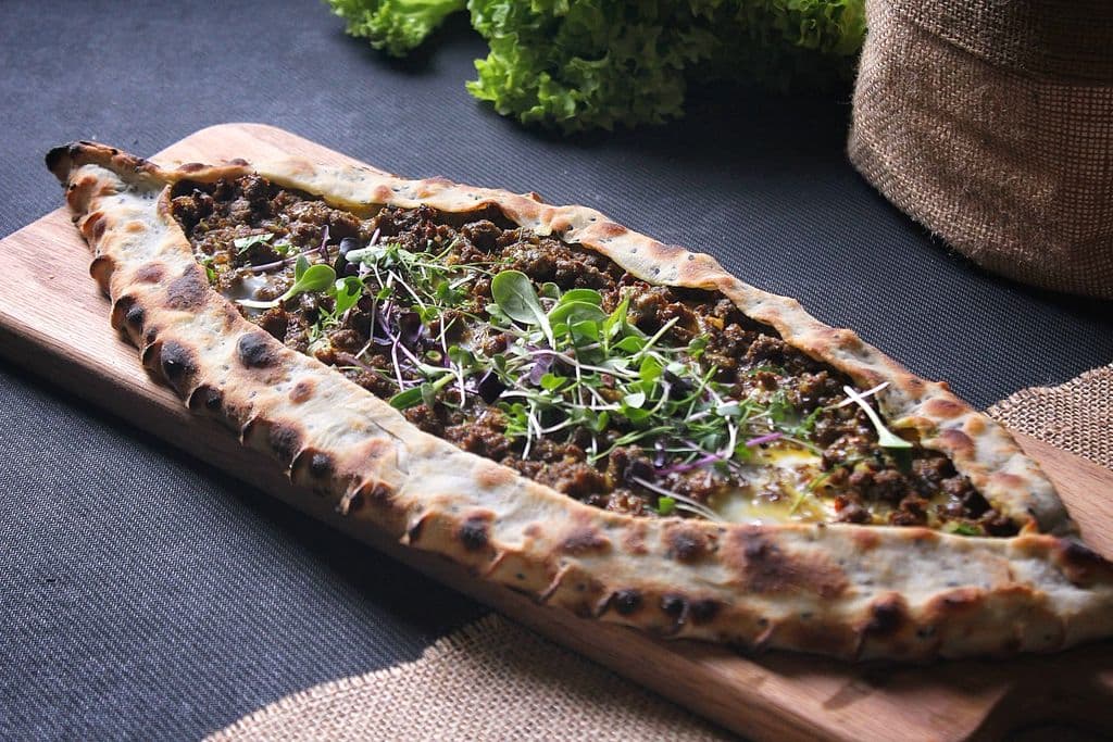 Turkish pide with minced meat and greens on a board, by Shameel mukkath