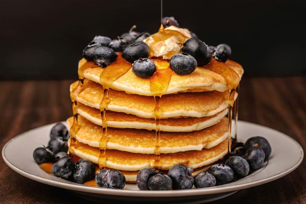 Stack of pancakes with blueberries and syrup, by Amber Fisher