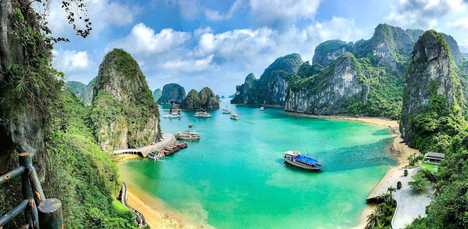 Boats on turquoise water below limestone karsts in Ha Long Bay, by Marina Lobato