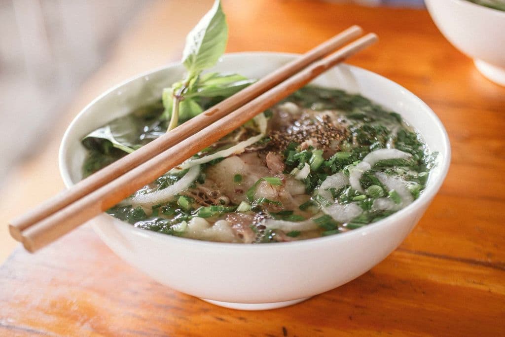 Bowl of Vietnamese phở with beef, herbs and chopsticks, by Nam Phong Bùi